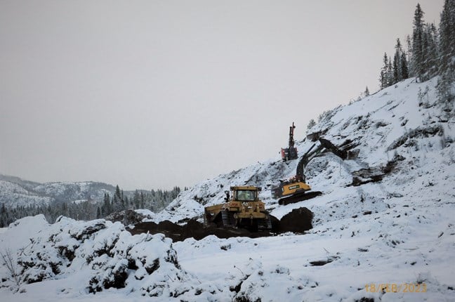 Bildet viser borerigg og gravemaskiner i aktivitet i en snødekt bergside. Bildetekst: Det pågår boring, sprengning og masseforflytning på Jensmyra. Foto: Statens vegvesen.
