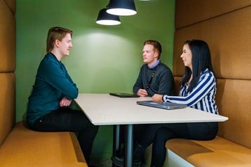 Tre personer sitter rundt et bord i et kontorlandskap