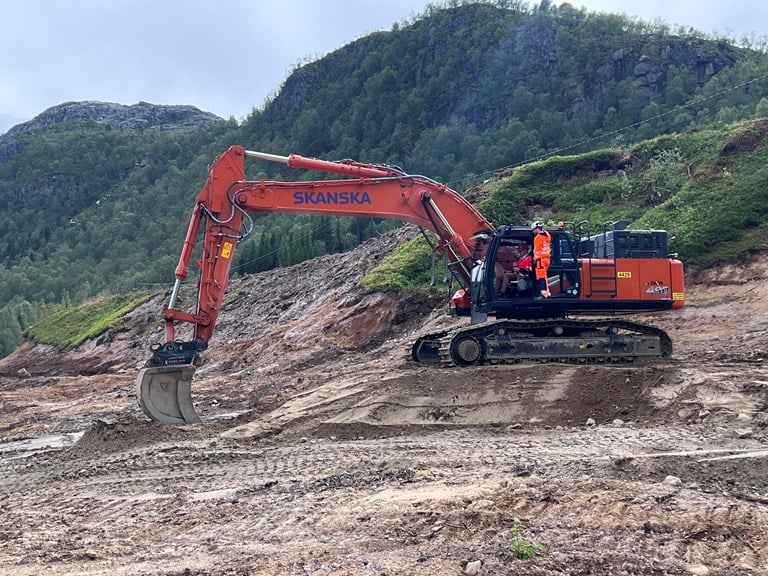Bildet viser Samferdselsministeren i en gravemaskin, som graver i et jordsmonn for å symbolisere første spadetak på OPS-prosjektet E10/rv.85 Tjeldsund–Gullesfjordbotn–Langvassbukt