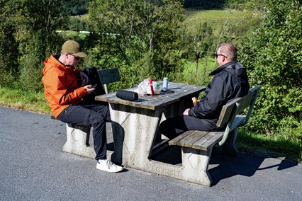 To menn spiser ved benk og bord på rasteplass