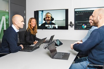 Fire personer rundt et bord i møte med en på skjermen 