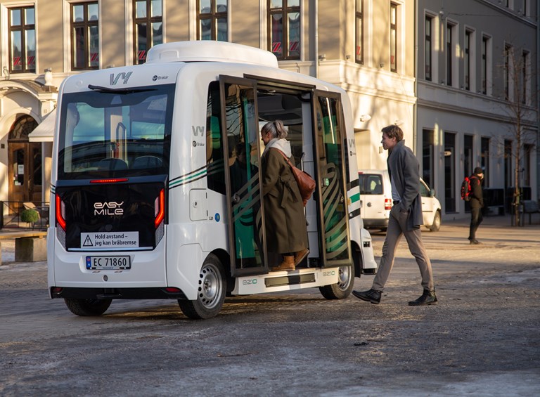 Passasjerer går på en selvkjørende buss i et bymiljø.