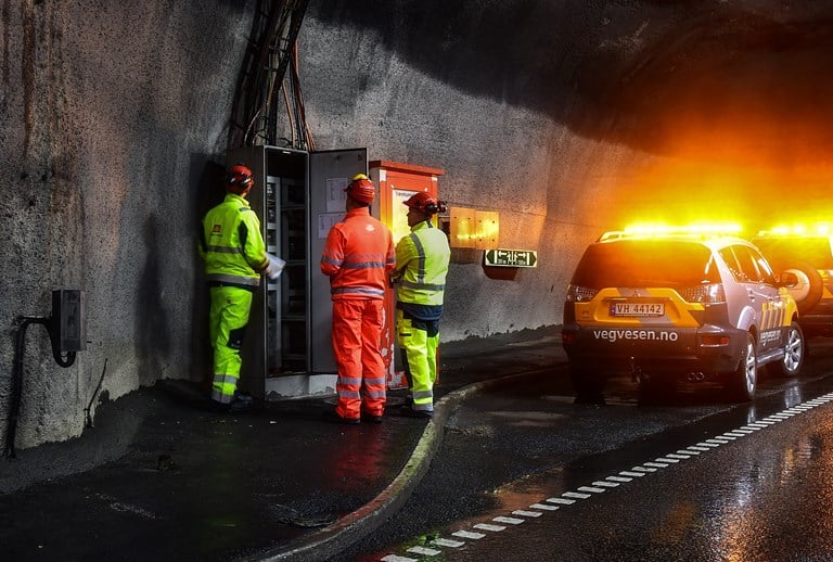 Tre personer i arbeidsklær inspiserer et elektroskap i en tunnel.