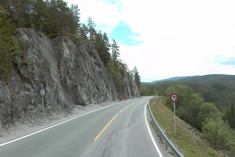 Veg med bratt fjellskjæring på eine sida og bratt skråning på den andre.