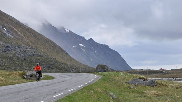 Syklist på veg med fjell og fjord i bakgrunnen.