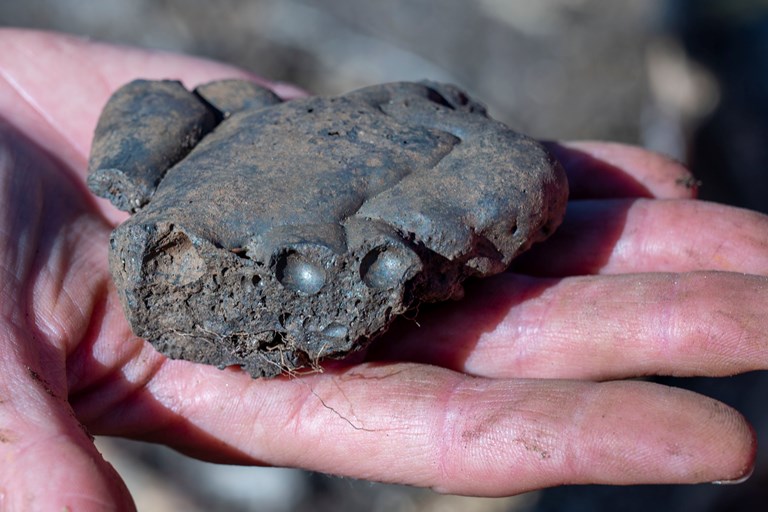 Ein klump av slagg frå jernproduksjon, i handa på arkeologen - bilde