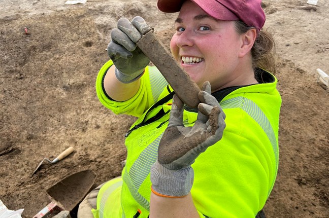 En av arkeologene fra Kulturhistorisk museum viser fram et flott bryne som ble funnet i hustufta.