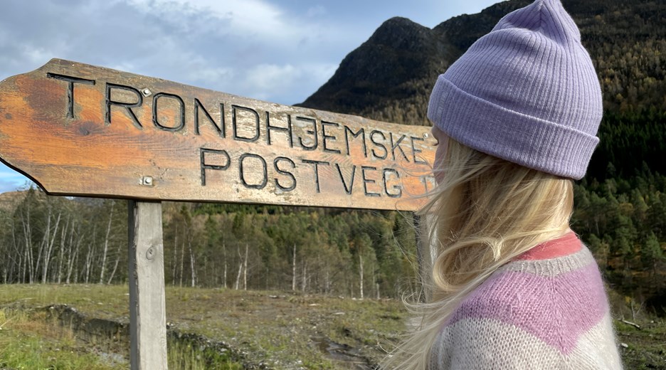 Fotturist på Ørskogfjellet ved et skilt det står Trondhjemske postveg på - bilde